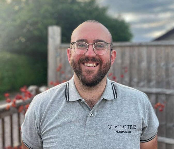 Man wearing a gray polo shirt with 'Quatro Tiles Monmouth' logo outdoors.